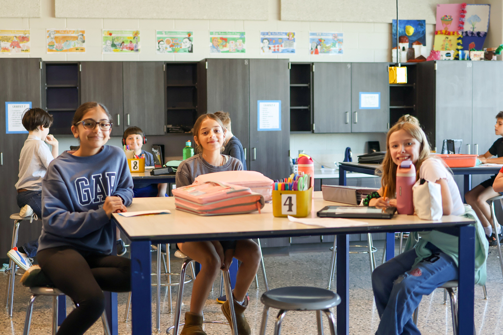 three girls pose for a photo at a table in a classroom