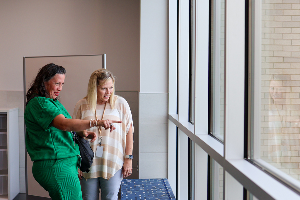 two women smile looking out a window of a school