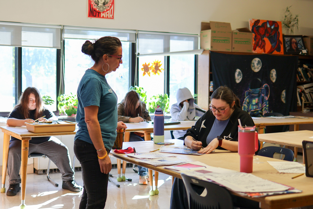 a teacher standing near a student at a desk in a classroom