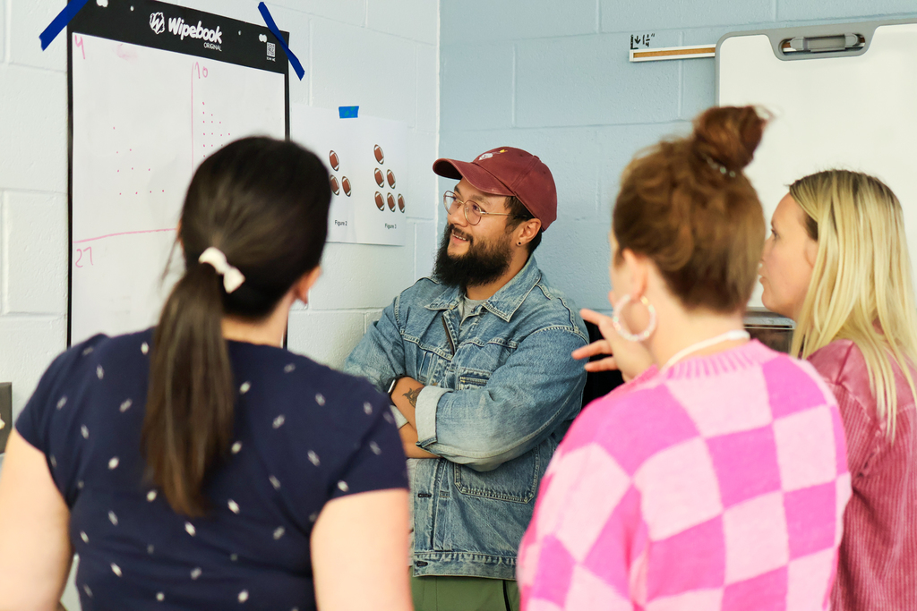 people stand around a white board looking at a math problem