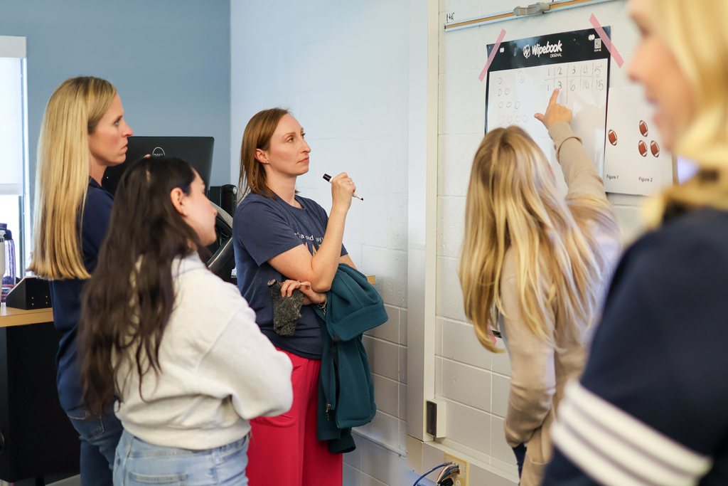 multiple women standing together working on a math problem on a white board.