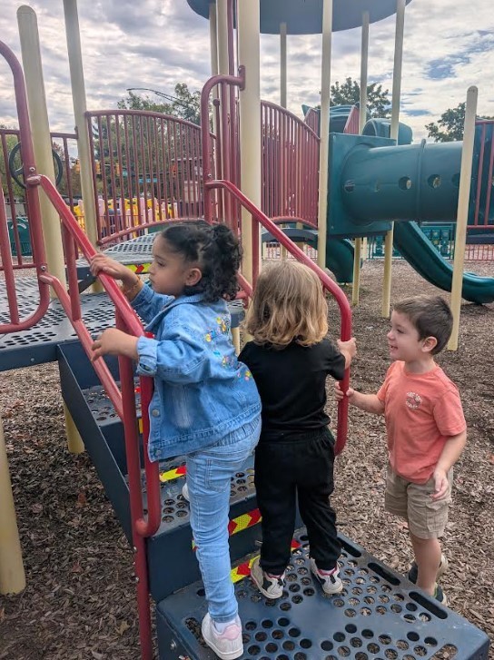 Three three year olds climbing on a play structure.