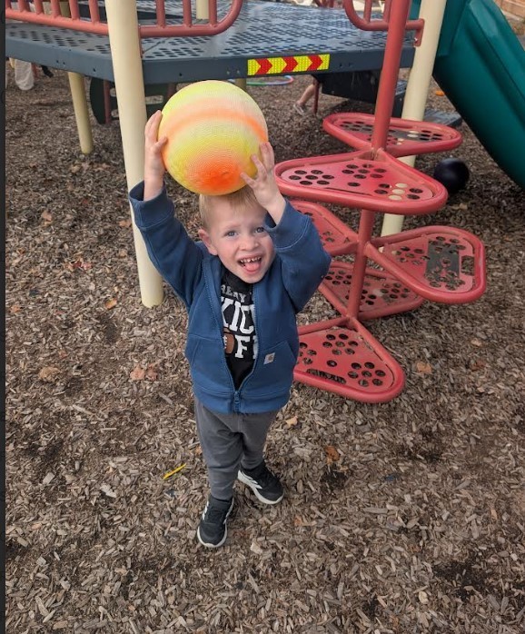 A young boy holding a ball above his head.