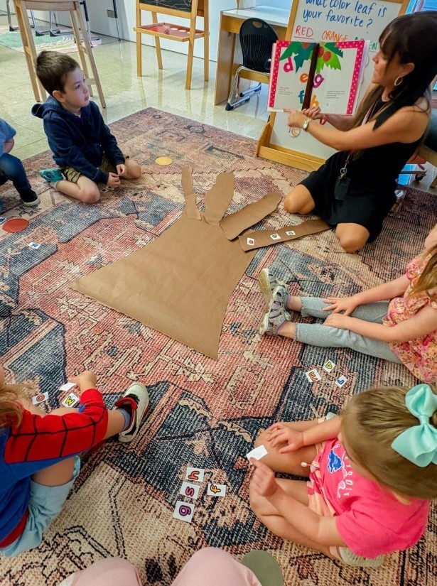 All the students sitting at a carpet listening to a story from their teacher.