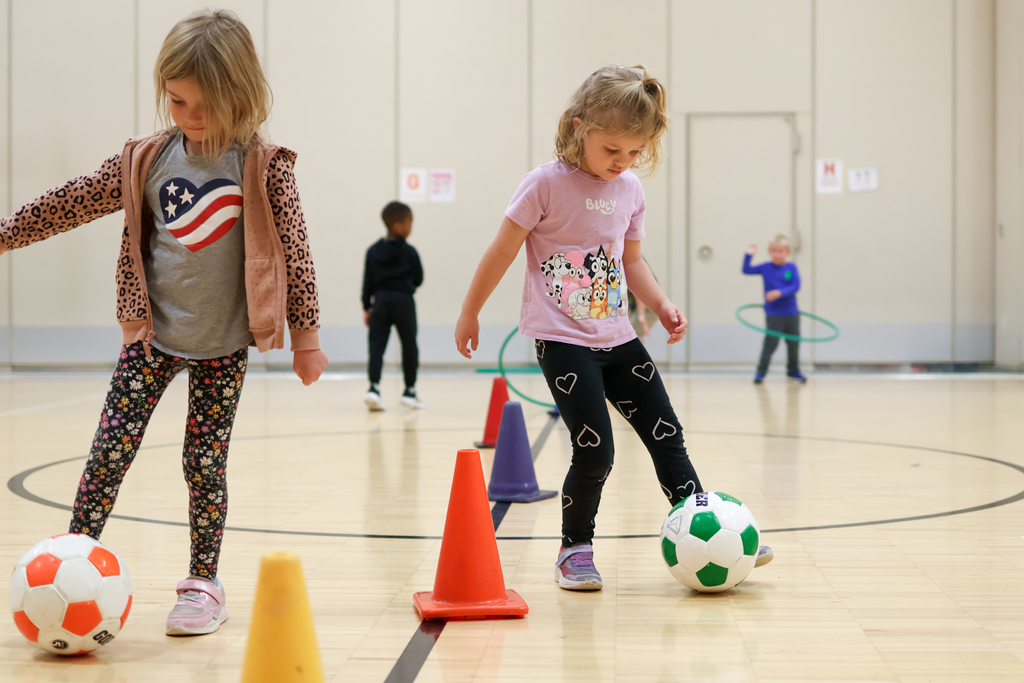 two girls kicking soccer balls in a gym