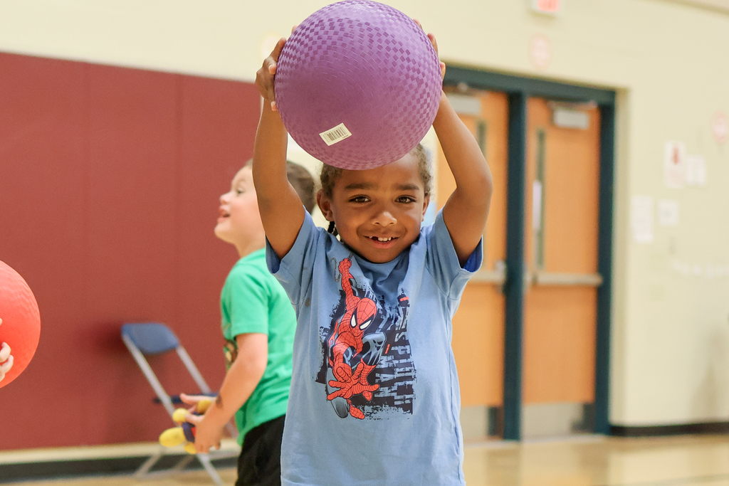 a boy holding a ball above his head and smiling