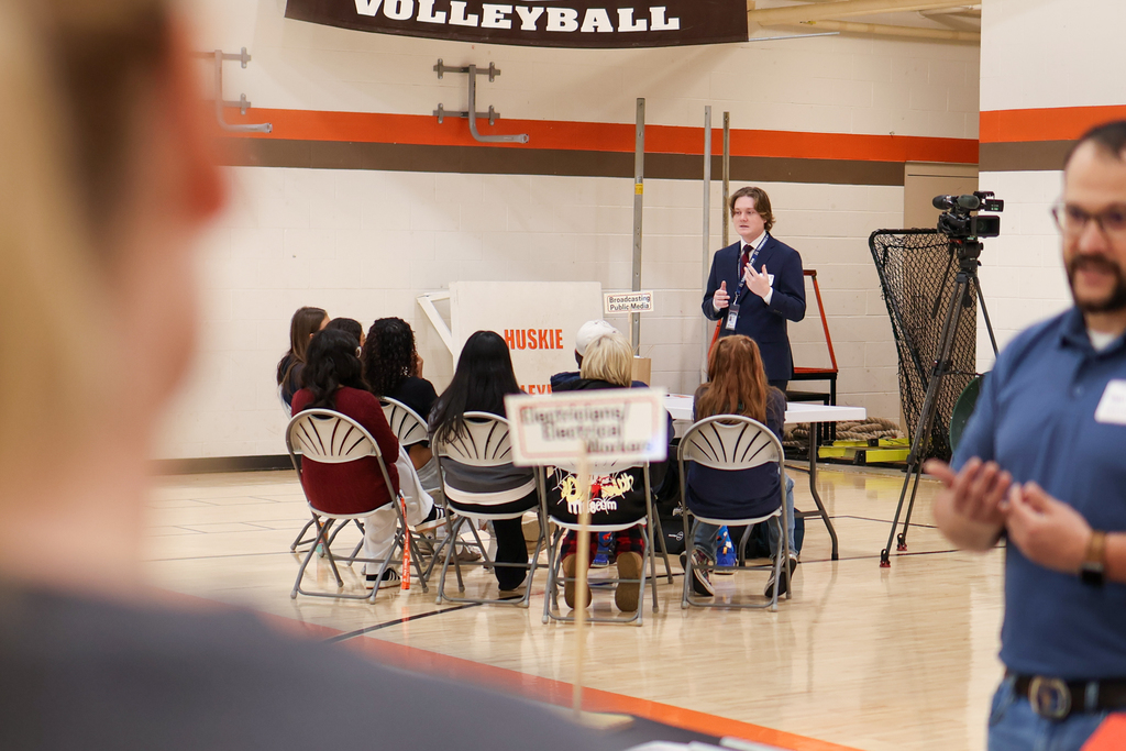 a broadcast journalism speaks to students gathered in a gym