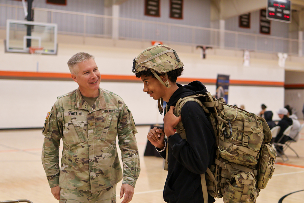 a student trying on army gear standing near an officer in a gym