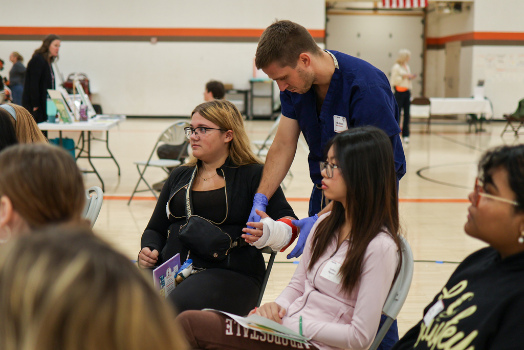 a doctor bandages up a girl's arm during a presentation in a school gym