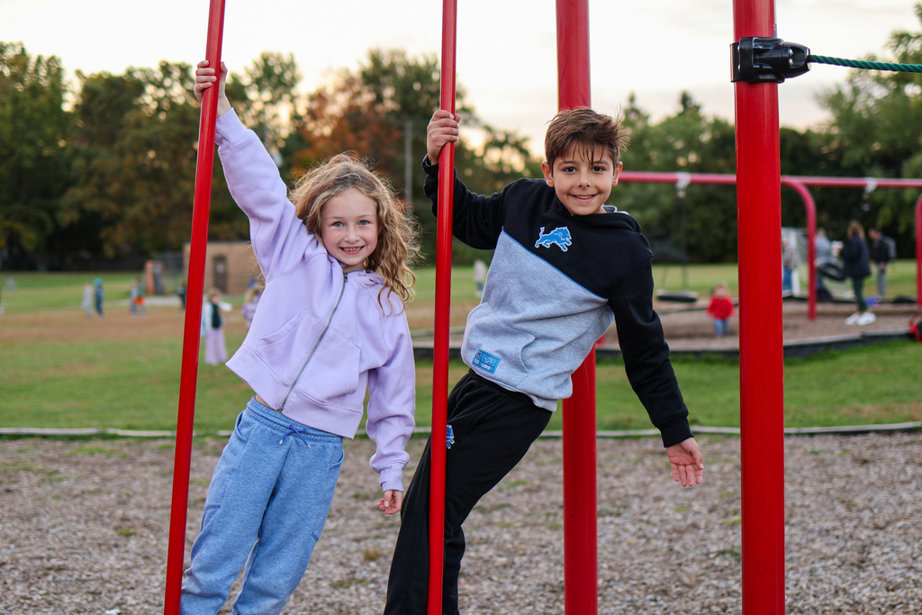 two kids hanging on playground equipment smiling for a photo
