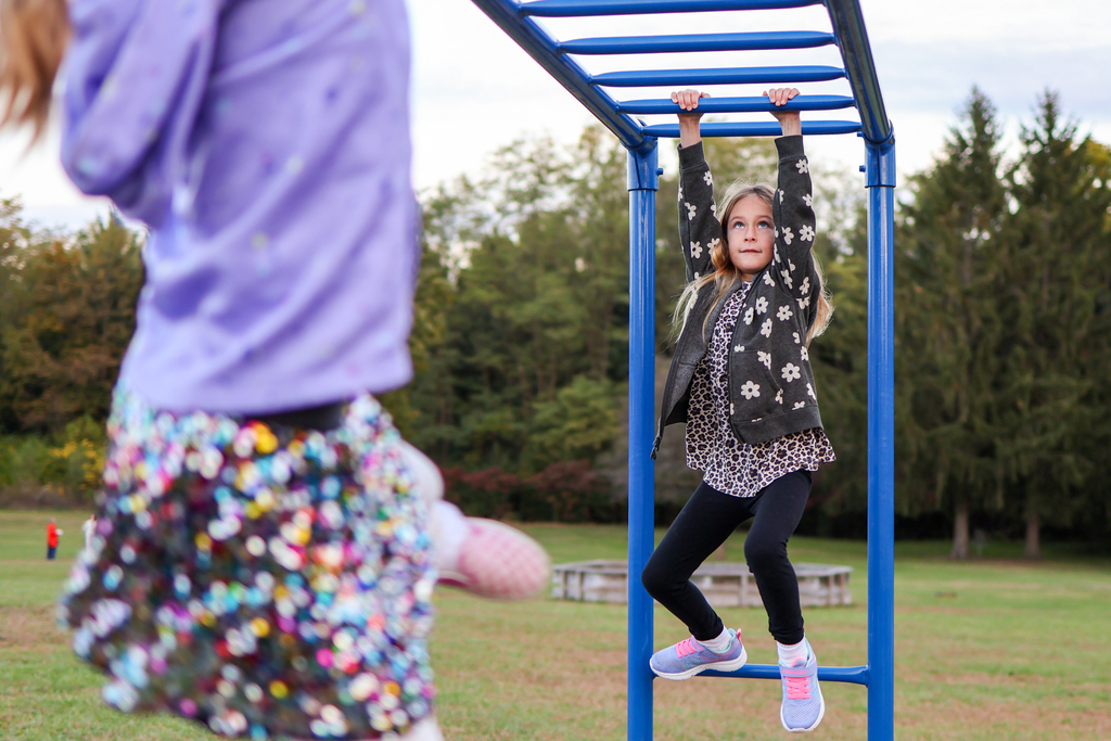 a girl crossing the monkey bars outside on a playground