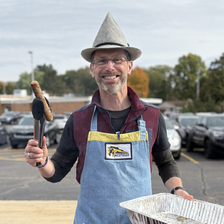 a man holding a brat grilling outside