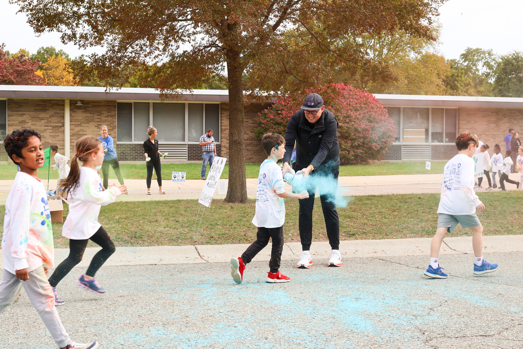 a man spraying blue powder on students as they run by