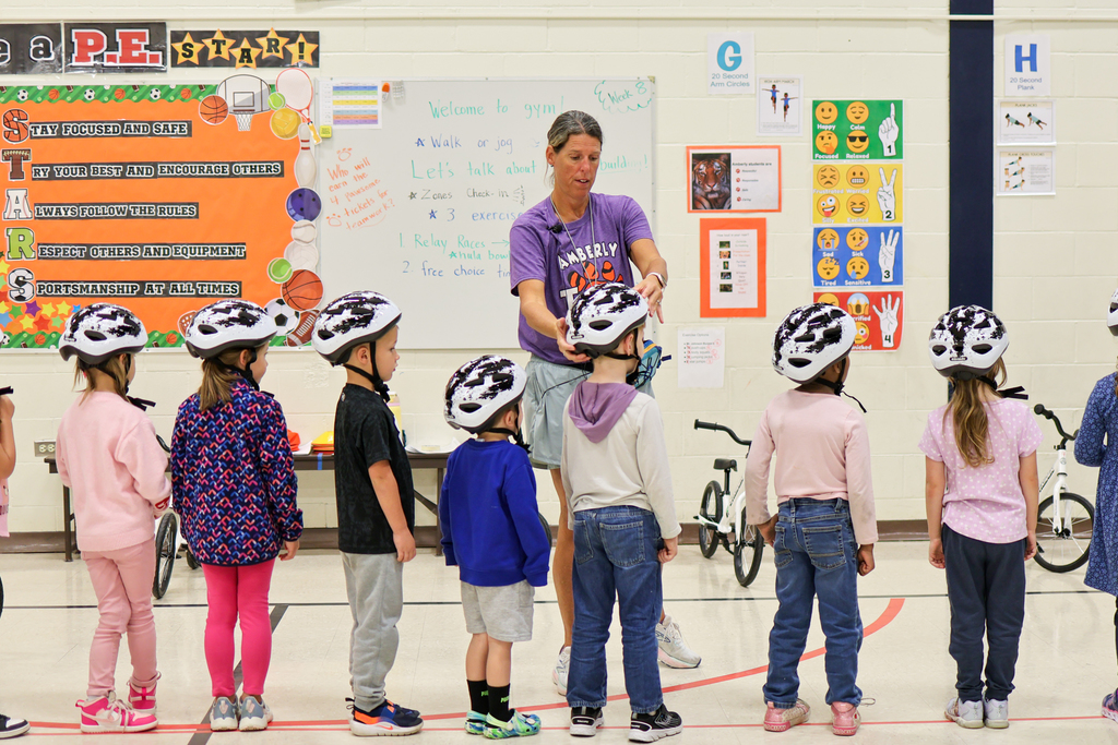 a teacher adjusts bike helmets on students in a gym