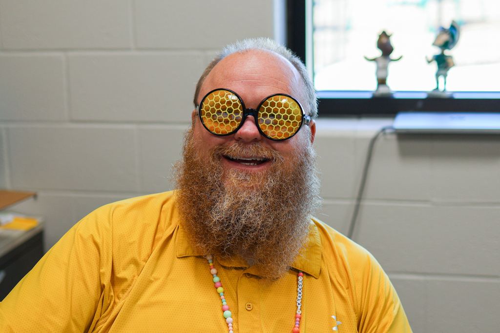 a man smiling for a photo wearing sunglasses that have bee hive on them. 