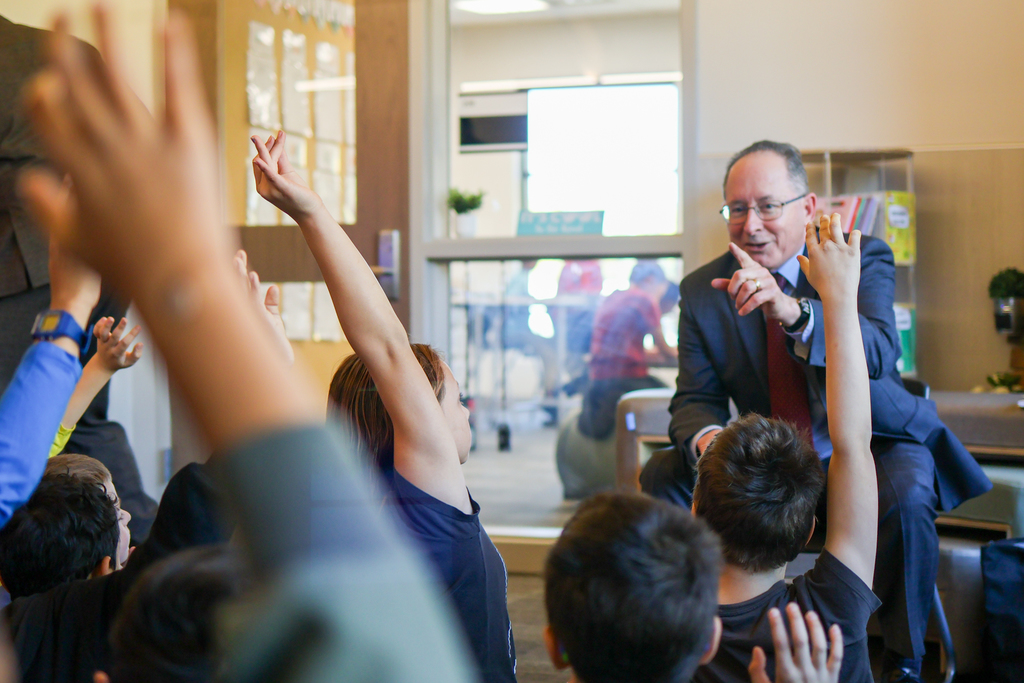 a man points at children holding their hands up 