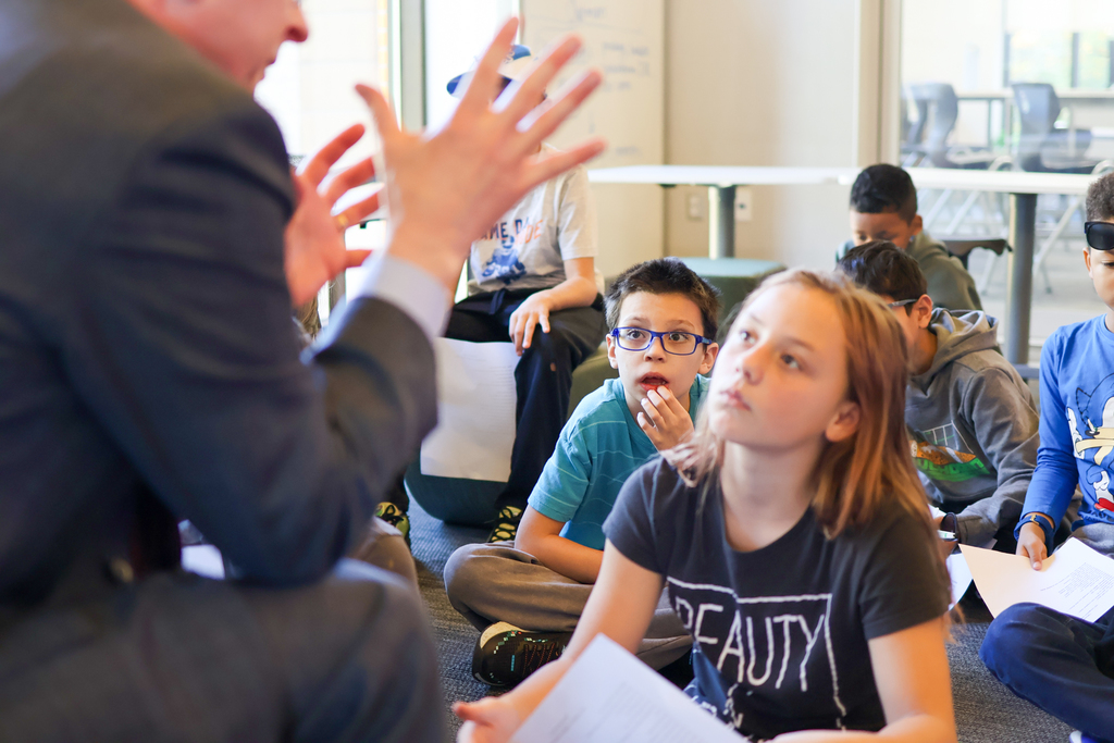 kids sitting on the floor listening to a man speak