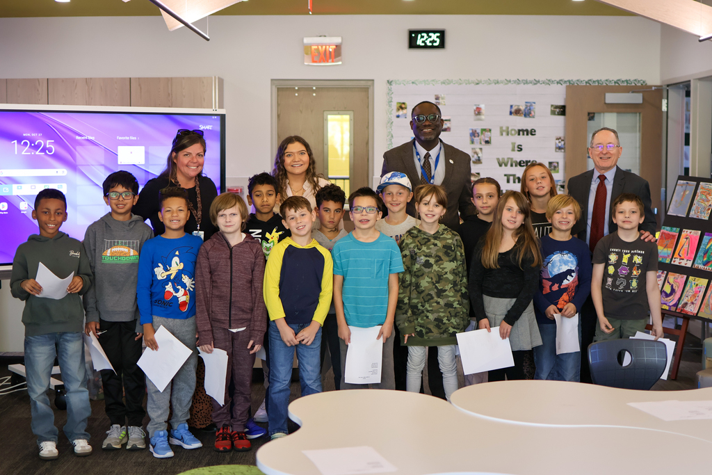 a large group of students posing for a photo with adults in a classroom