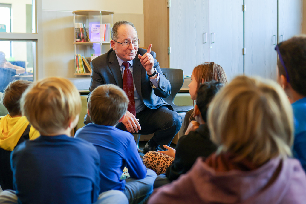 a man sitting on a chair speaking to a group of students