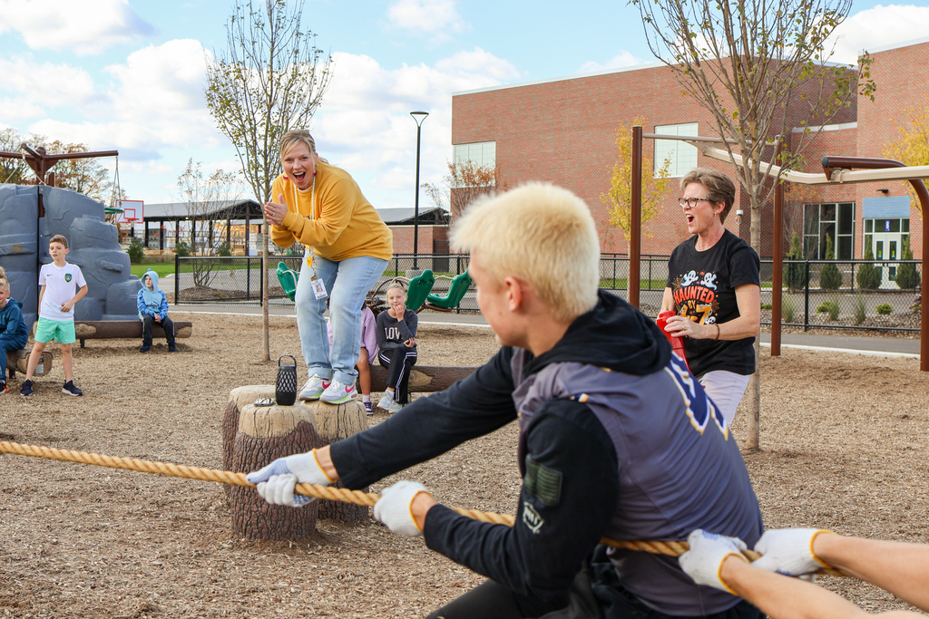 two women cheer as students play tug-of-war outside on a playground