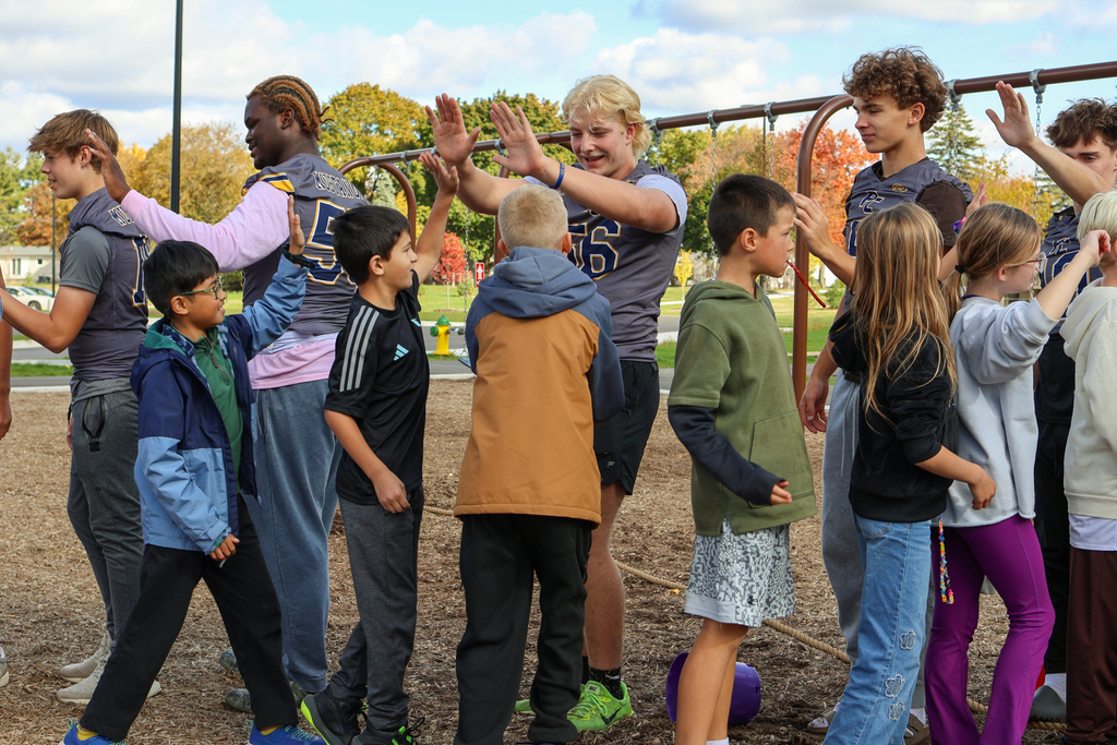 elementary students high five high school football players outside on a playground