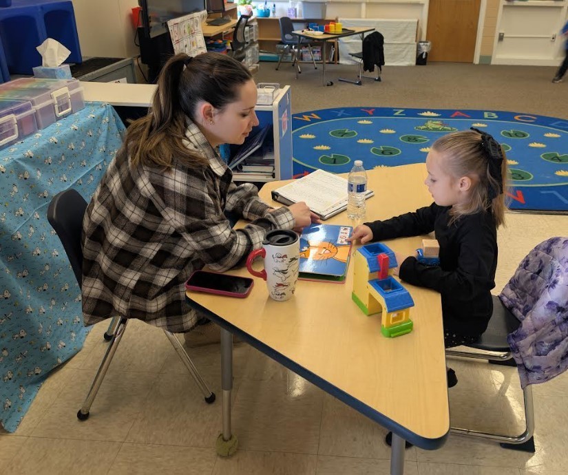 Student and speech therapist sitting at a table together.
