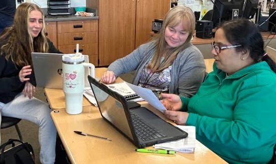 Three teachers helping on a computer together.