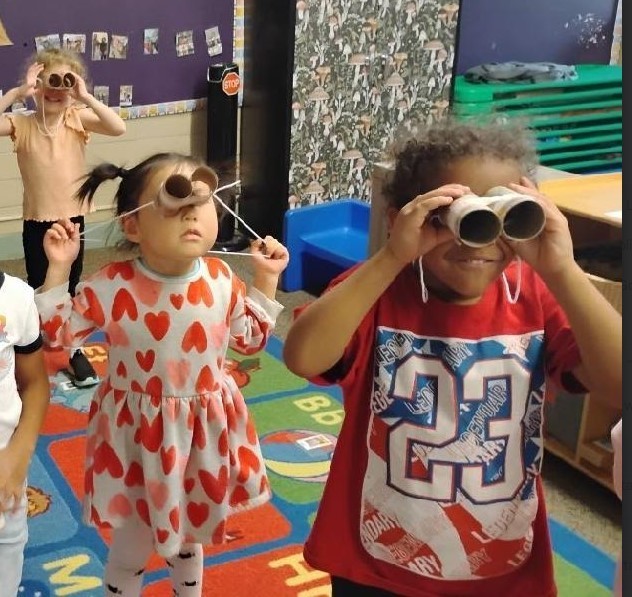 Three students holding binaculars and looking away,