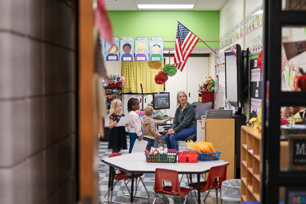 students and a teacher inside a classroom under an American Flag