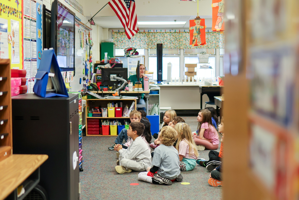 students sitting on the floor of a classroom looking up at a tv