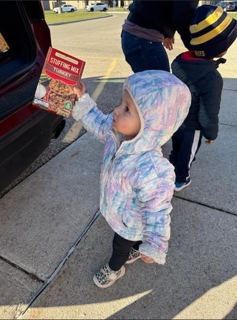 A little girl handing a box to an adult.