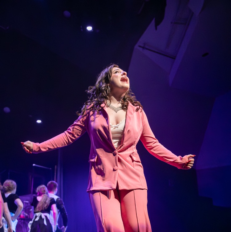 a girl in a pink suit singing on a stage