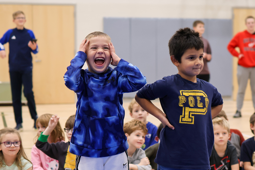 two boys smiling in a gym with kids behind them