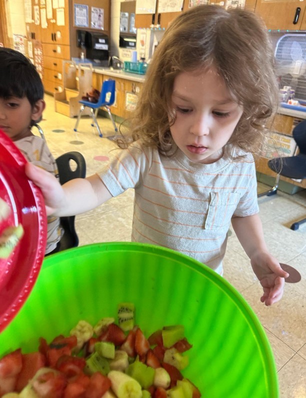 A little boy mixing fruit in a bowl.