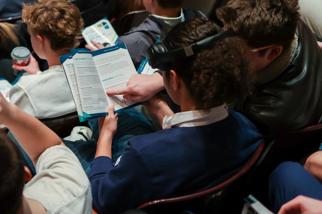 students sitting in an auditorium looking at a booklet of course offerings