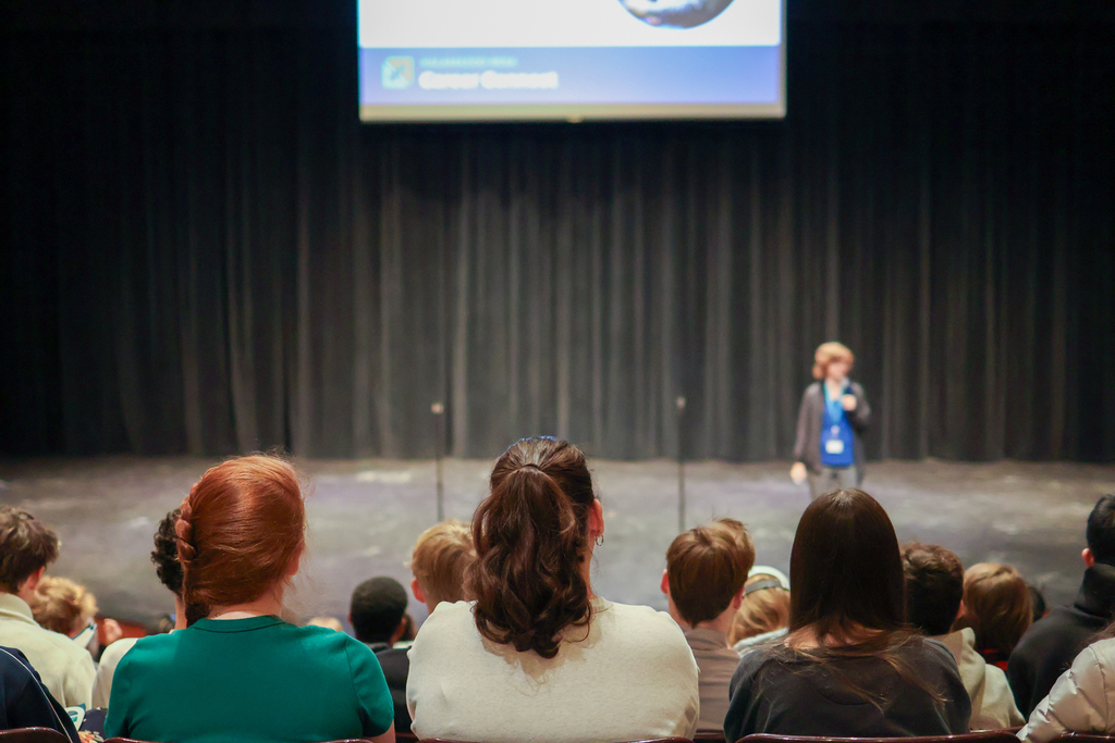 students listening in an auditorium to a woman speaking on stage