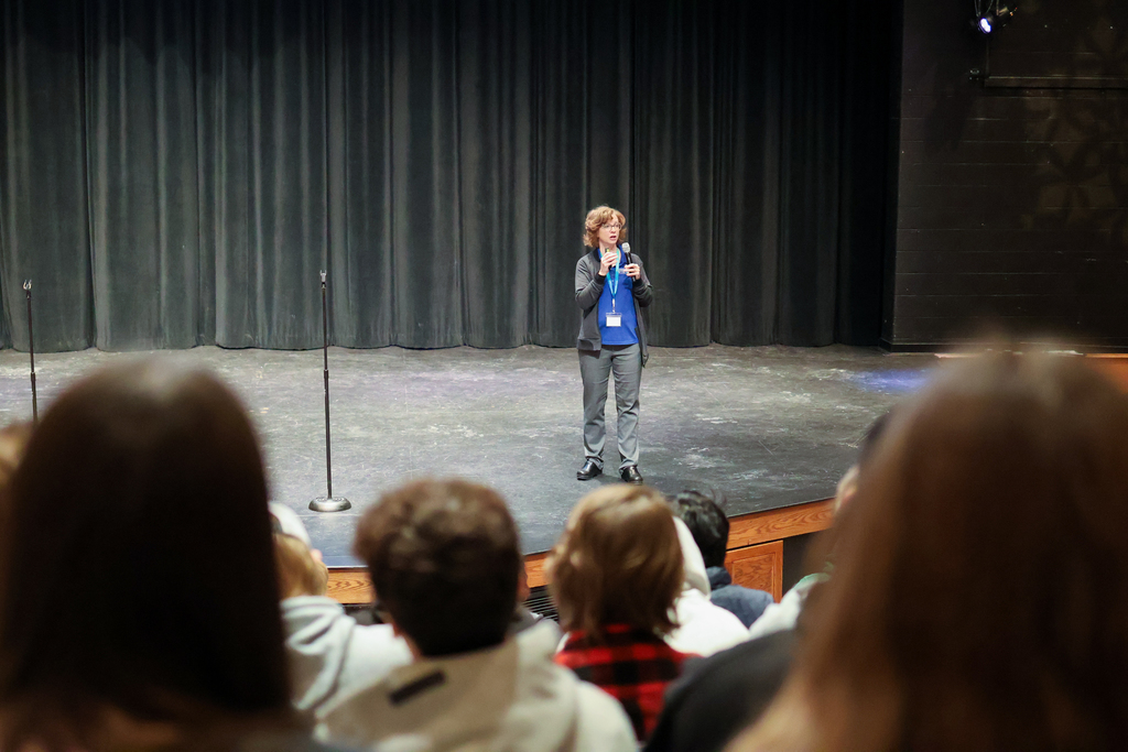 a woman speaks on stage in front of students in an auditorium