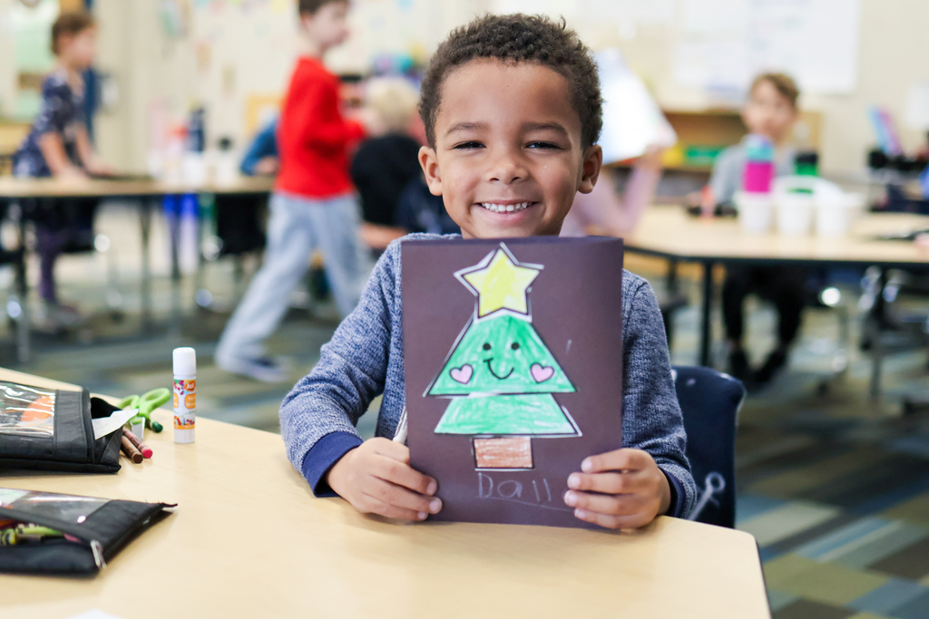 a little boy holding his card smiles in a classroom