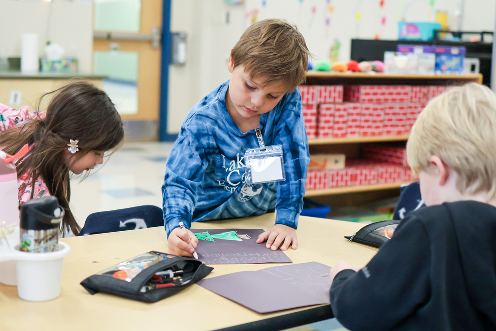 a boy working on a craft at his desk in a classroom