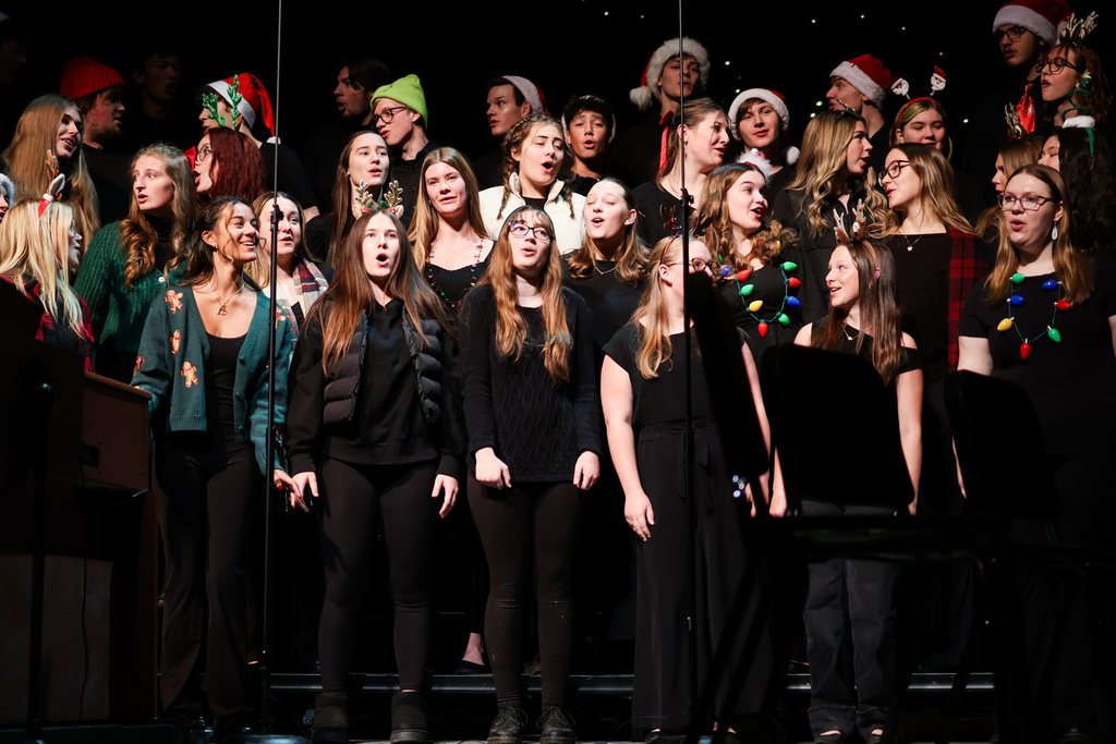 a choir of students wearing holiday gear singing on stage