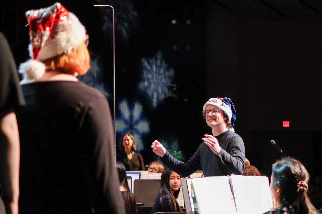 a man wearing a santa hat directing a choir on stage