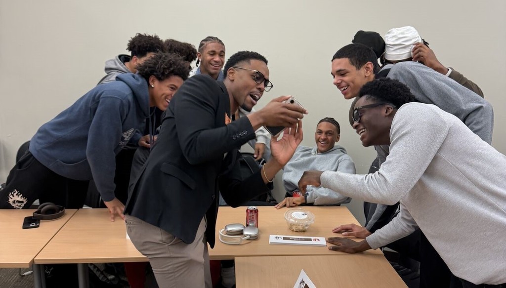 a man showing a group of high school boys something on his phone. 