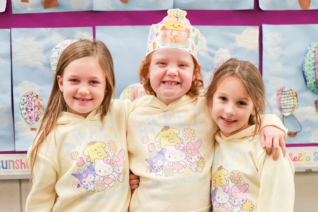 three girls dressed in matching sweatshirts pose for a photo
