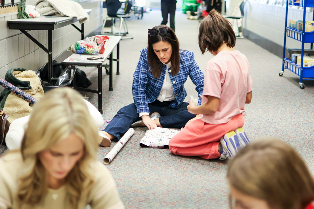 a woman and girl wrapping a gift on the floor of a hallway