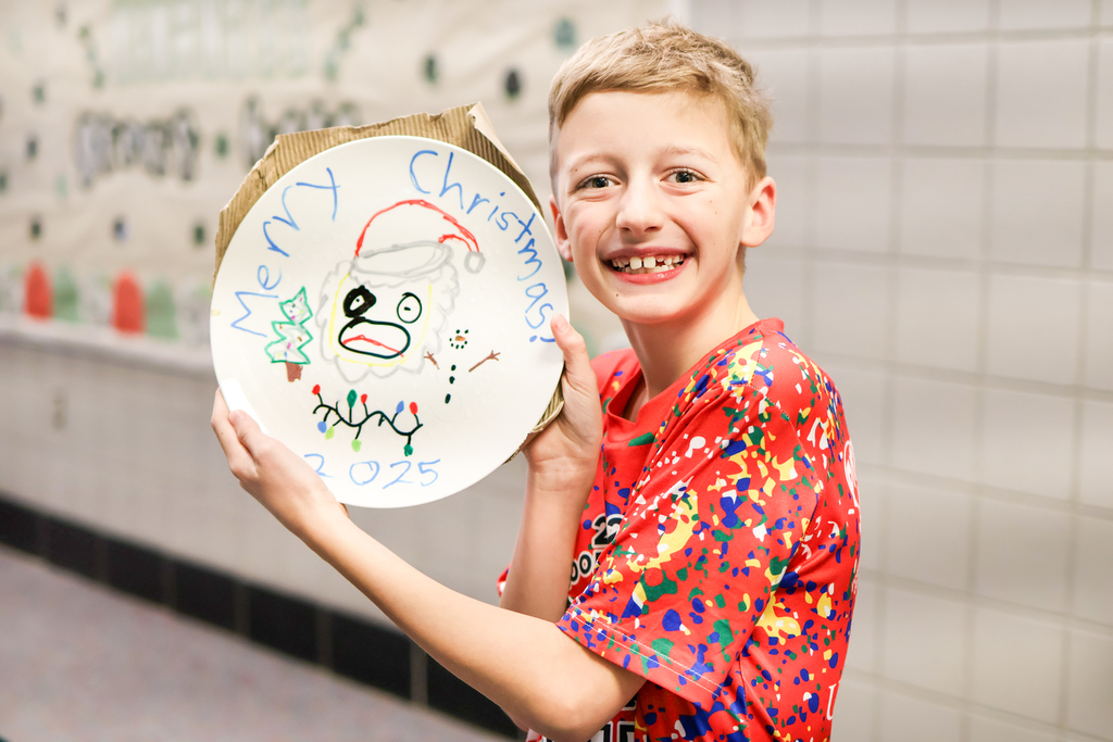 a boy smiles for a photo holding up a hand painted plate