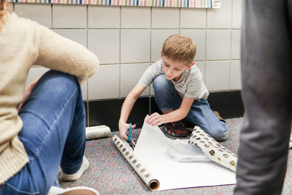 a boy cutting wrapping paper on the floor