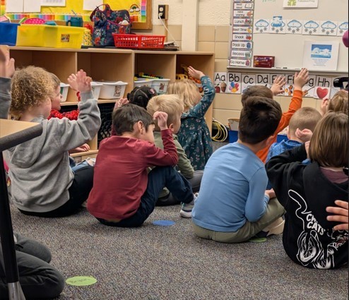 Students sitting at the carpet together listening to a music lesson.