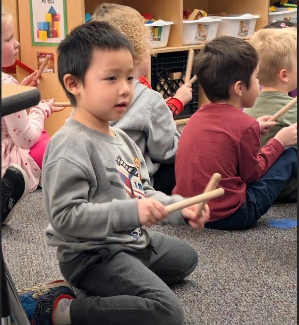 A four year old boy holding music sticks together.