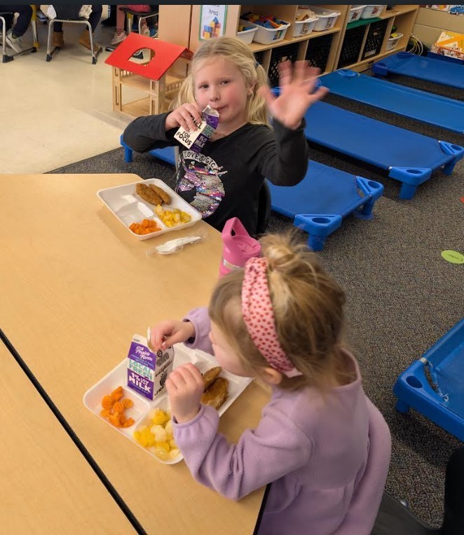 Two girls eating lunch together at a table.