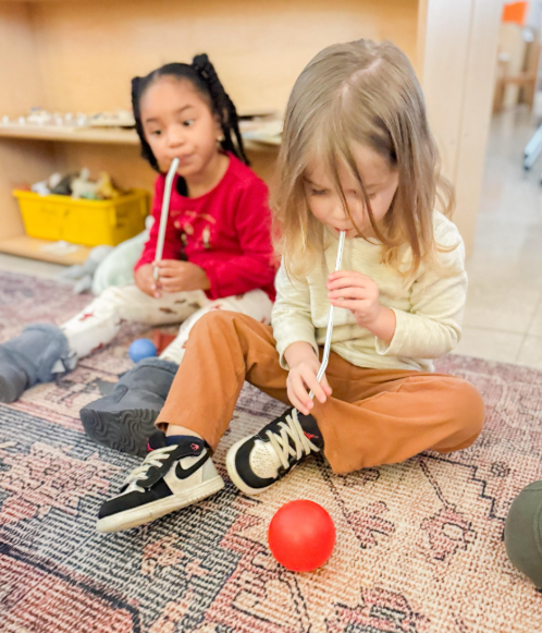 A boy and a girl using a straw to move a small ball.